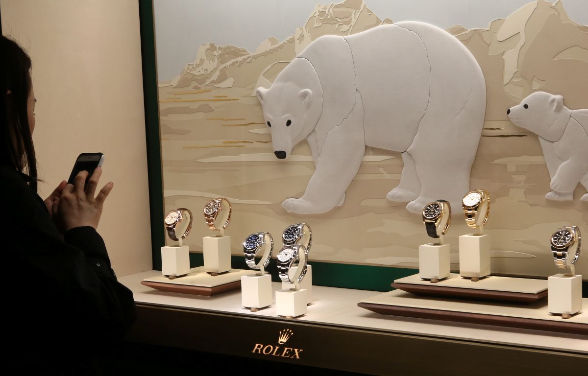 Vitrine onde estão seis relógios Rolex e uma mulher do lado de fora fotografando