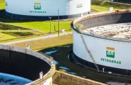A imagem mostra dois tanques brancos de armazenamento da Petrobras em uma área externa gramada, cercados, com tubulações vermelhas e postes de iluminação.