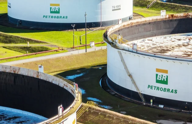 A imagem mostra dois tanques brancos de armazenamento da Petrobras em uma área externa gramada, cercados, com tubulações vermelhas e postes de iluminação.