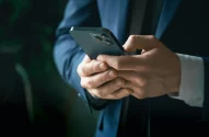 Em um ambiente interno suavemente iluminado, uma pessoa em um terno azul escuro segura um celular moderno com múltiplas lentes. A imagem será utilizada para ilustrar conteúdo sobre a investigação do Pix aberta pelos EUA