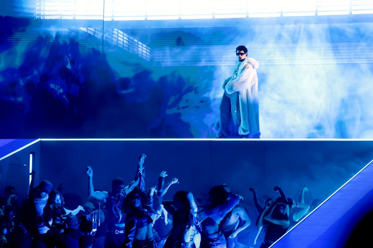 Imagem do cantor Bad Bunny, que está em cima de um palco azul, com a plateia logo abaixo dele