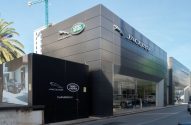 Imagem da fachada da Jaguar Land Rover, um prédio baixo marrom claro com o logotipo prateado