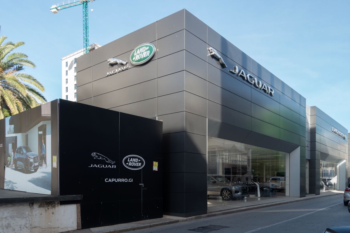Imagem da fachada da Jaguar Land Rover, um prédio baixo marrom claro com o logotipo prateado
