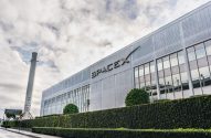 Fachada da SpaceX, com letras cinzas em um prédio baixo branco, céu está cheio de nuvens