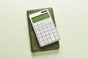 Calculadora branca sobre caderno verde, em fundo claro, com composição minimalista e iluminação suave. parcelar imposto de renda