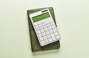 Calculadora branca sobre caderno verde, em fundo claro, com composição minimalista e iluminação suave. parcelar imposto de renda