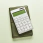 Calculadora branca sobre caderno verde, em fundo claro, com composição minimalista e iluminação suave. parcelar imposto de renda