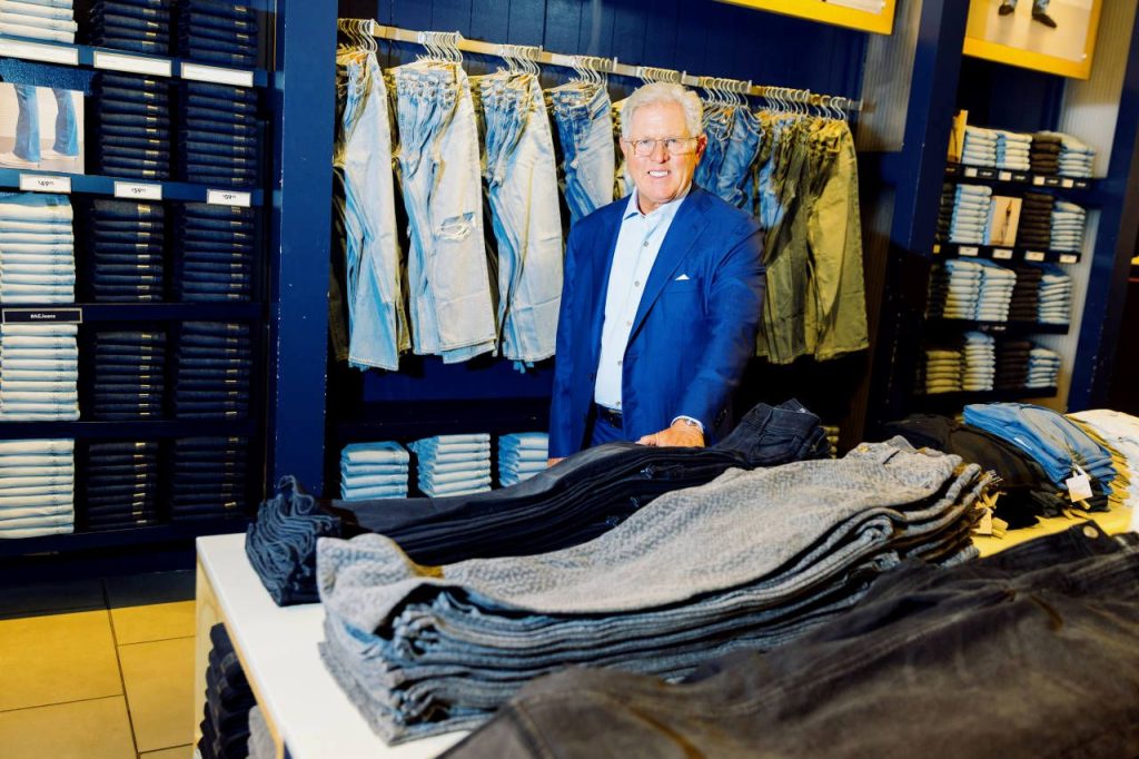 senhor de idade está de terno em frente a um balcão de roupas