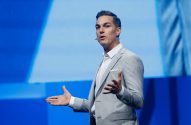 Foto do CEO da Electronic Arts: ele está de terno cinza, camisa branca em frente a um painel azul
