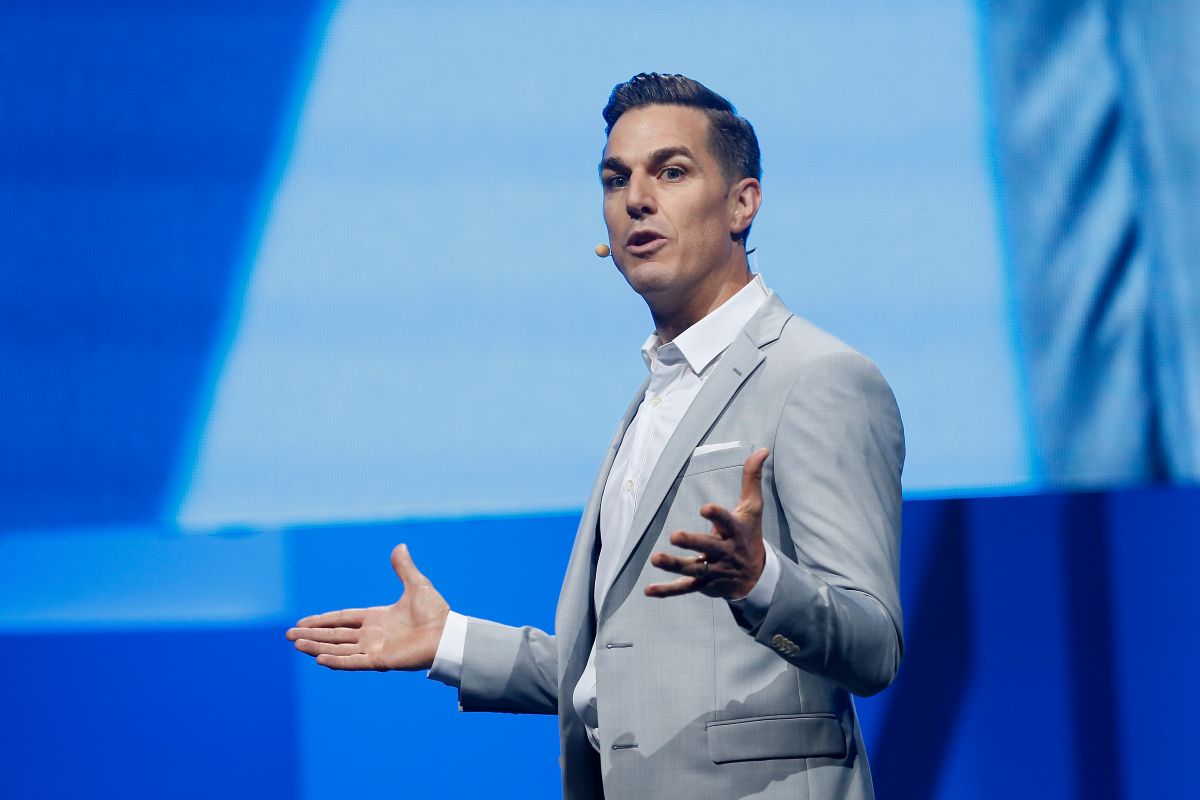 Foto do CEO da Electronic Arts: ele está de terno cinza, camisa branca em frente a um painel azul