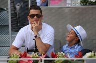 Cristiano Ronaldo está vendo um jogo, de camisa branca, óculos escuros, relógio e colar de ouro