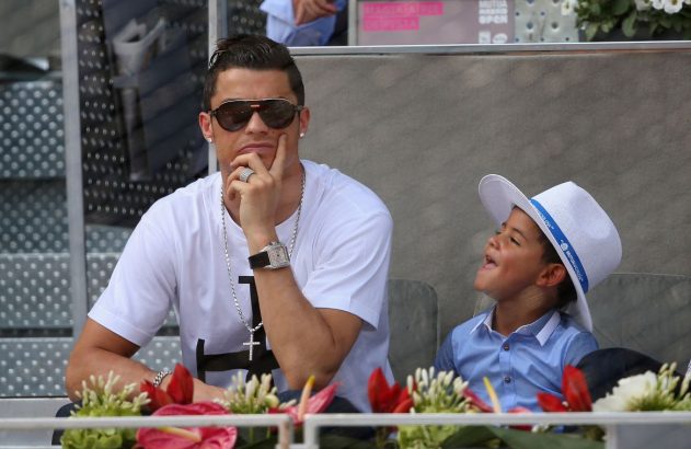 Cristiano Ronaldo está vendo um jogo, de camisa branca, óculos escuros, relógio e colar de ouro