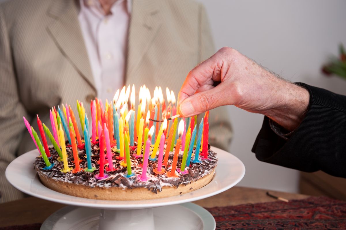 Um bolo cheio de velas é segurado pela mão de um homem mais velho, representando os supercentenários