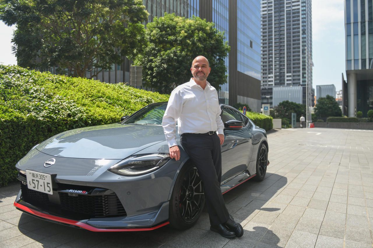 Executivo da Nissan está em pé enconstado em um carro da marca de camisa branca e calça preta