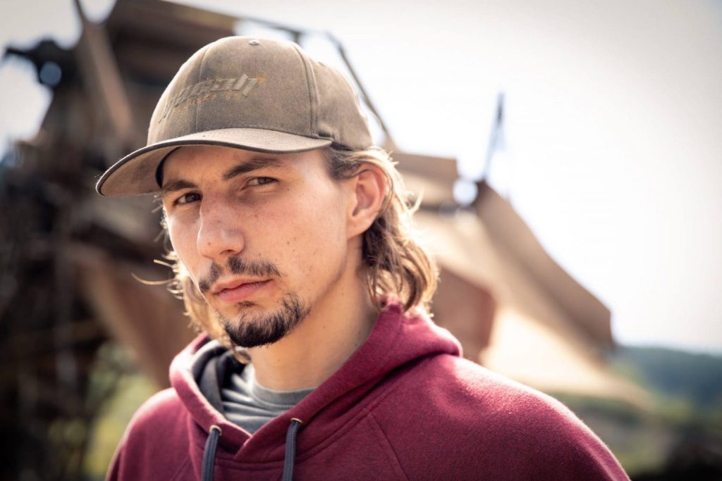 Parker Schnabel tem um programa sobre extração de ouro usa boné, cavanhaque e está de camisa vermelha