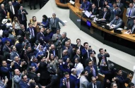 Plenário lotado com dezenas de parlamentares sorrindo e levantando celulares para registrar a comemoração após votação.