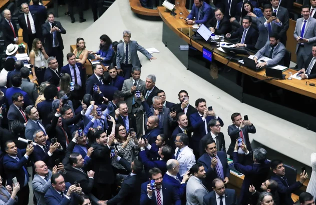 Plenário lotado com dezenas de parlamentares sorrindo e levantando celulares para registrar a comemoração após votação.