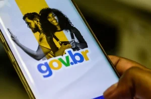 Smartphone com app gov.br aberto. Mão posiciona dedo para tocar botão "Entrar com gov.br". imposto de renda