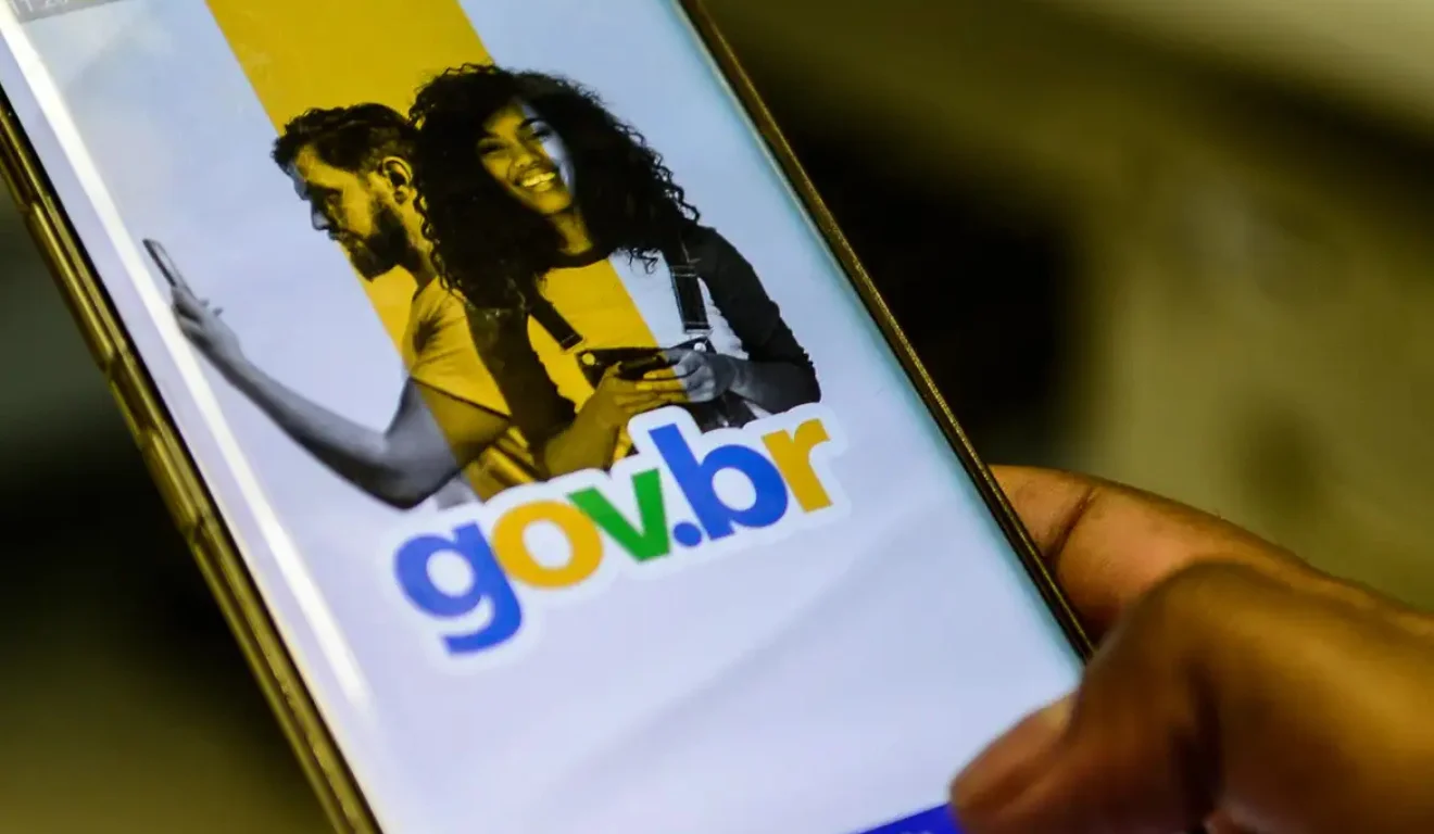 Smartphone com app gov.br aberto. Mão posiciona dedo para tocar botão "Entrar com gov.br". imposto de renda