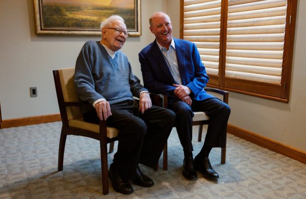 Warren Buffett e Greg Abel sorrindo em cadeiras.