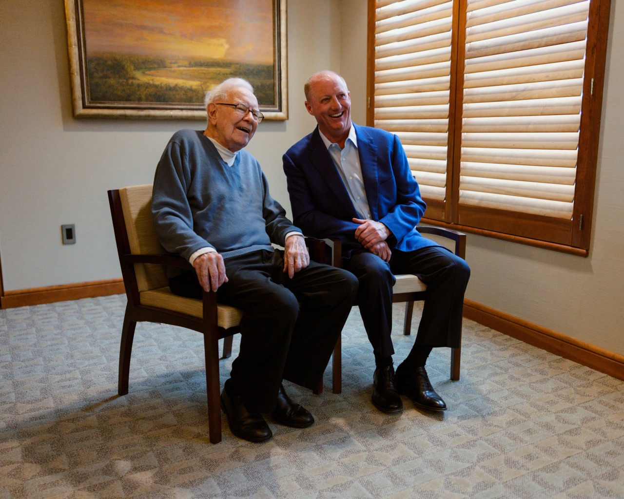 Warren Buffett e Greg Abel sorrindo em cadeiras.