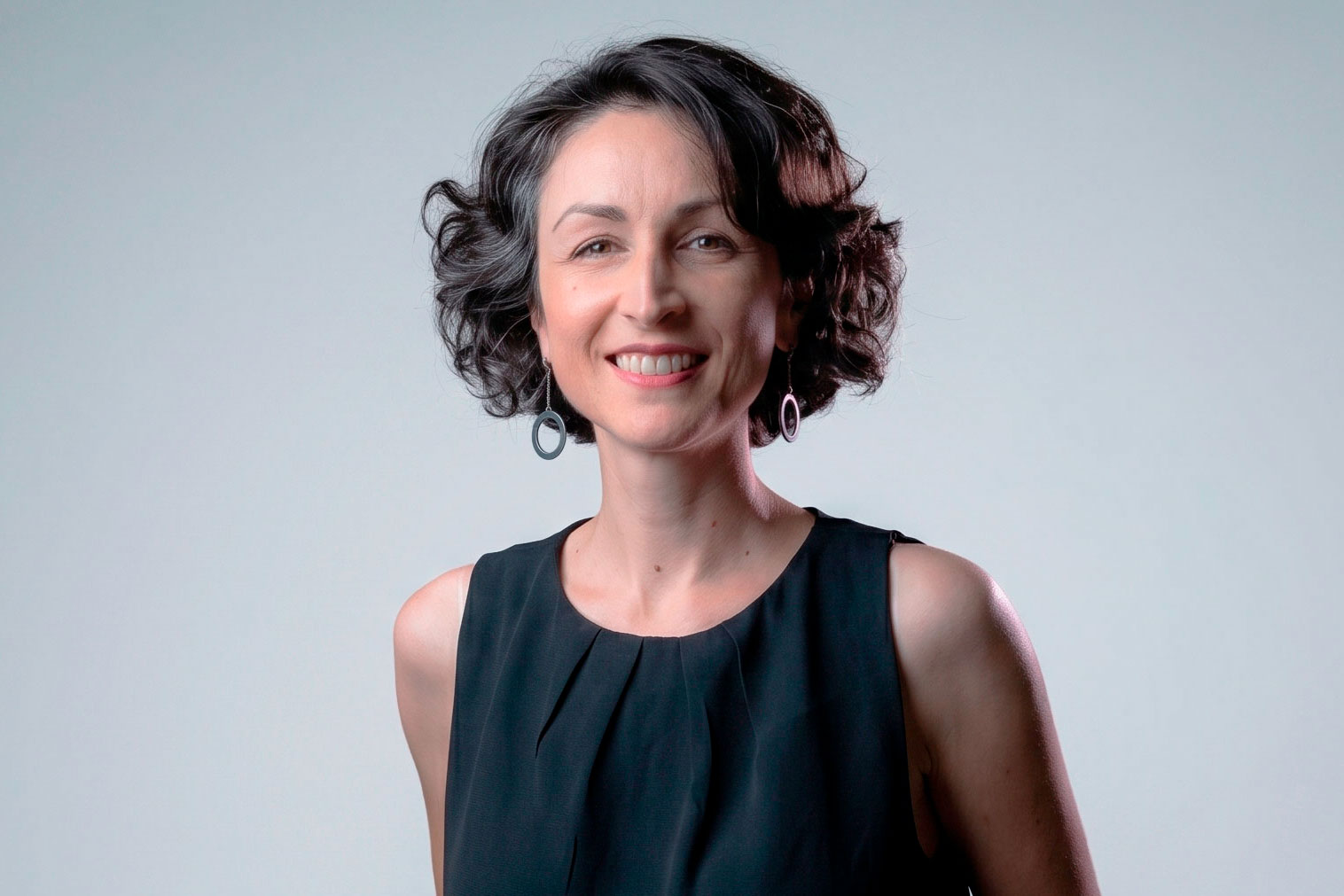 Jornalista Mariana Segala posa para foto de perfil corporativo em estúdio com fundo neutro e traje preto.