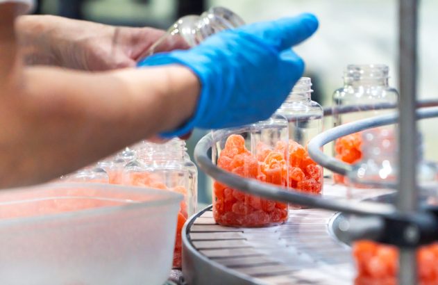 Funcionária farmacêutica em um controle de qualidade industrial verificando a produção de gomas nutricionais na fábrica