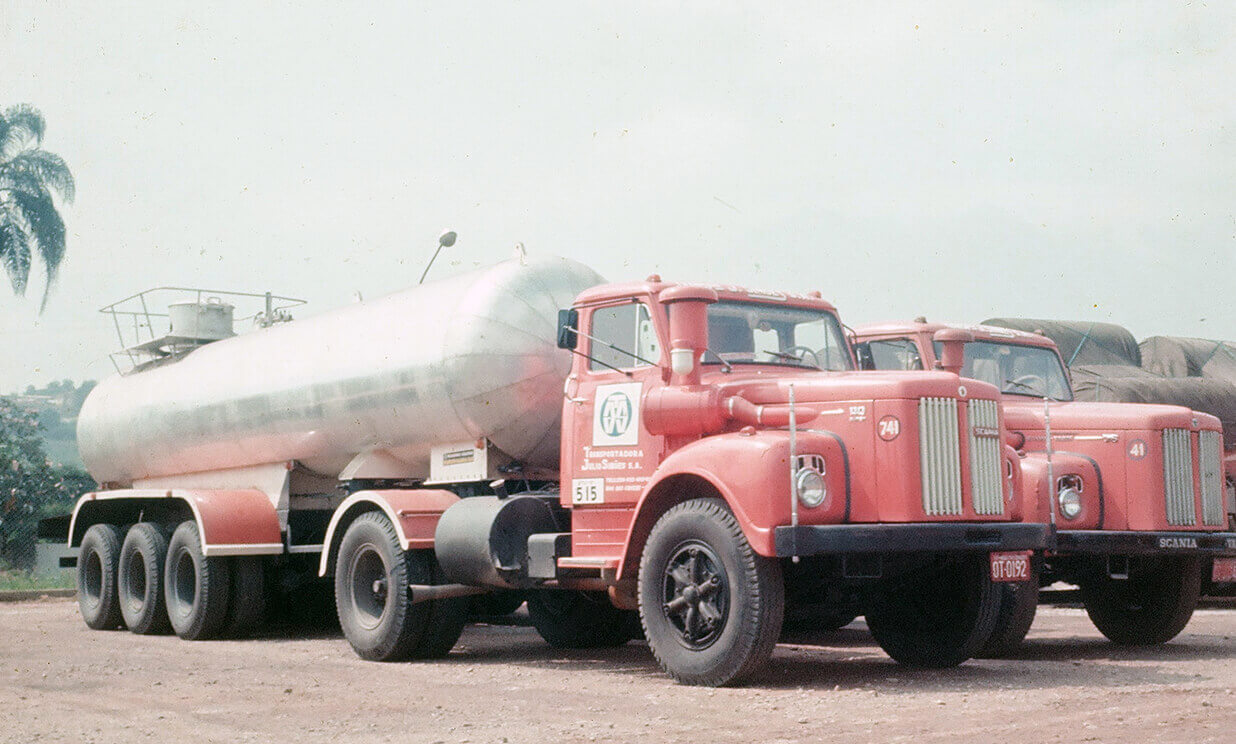Foto antiga mostra caminhões-tanque vermelhos da Transportadora Julio Simões estacionados em um pátio. Os veículos são modelos antigos da Scania e carregam o logo da JSL nas portas.