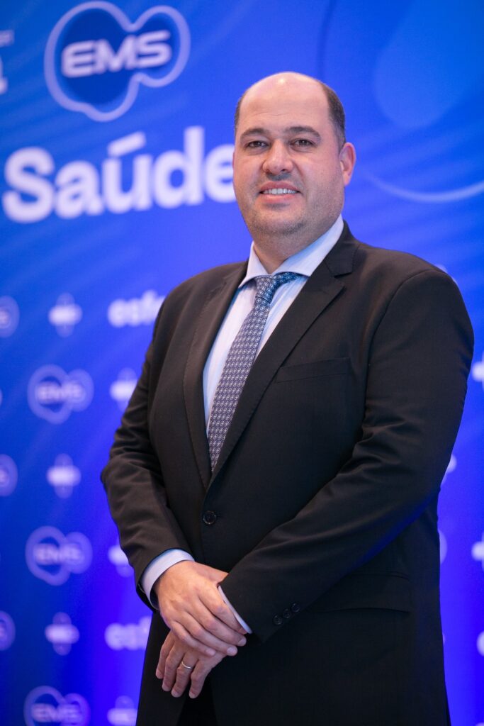 Marcus Sanchez de terno diante de painel azul com a marca EMS
