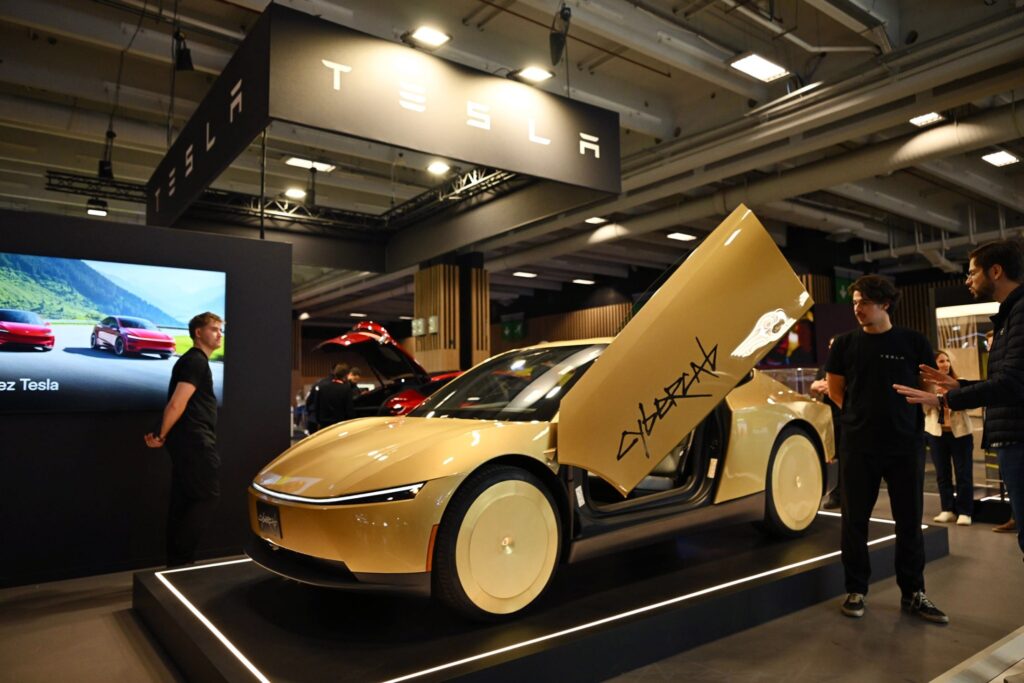 Cybercab dourado da Tesla em exposição, com uma porta levantada e visitantes ao redor.