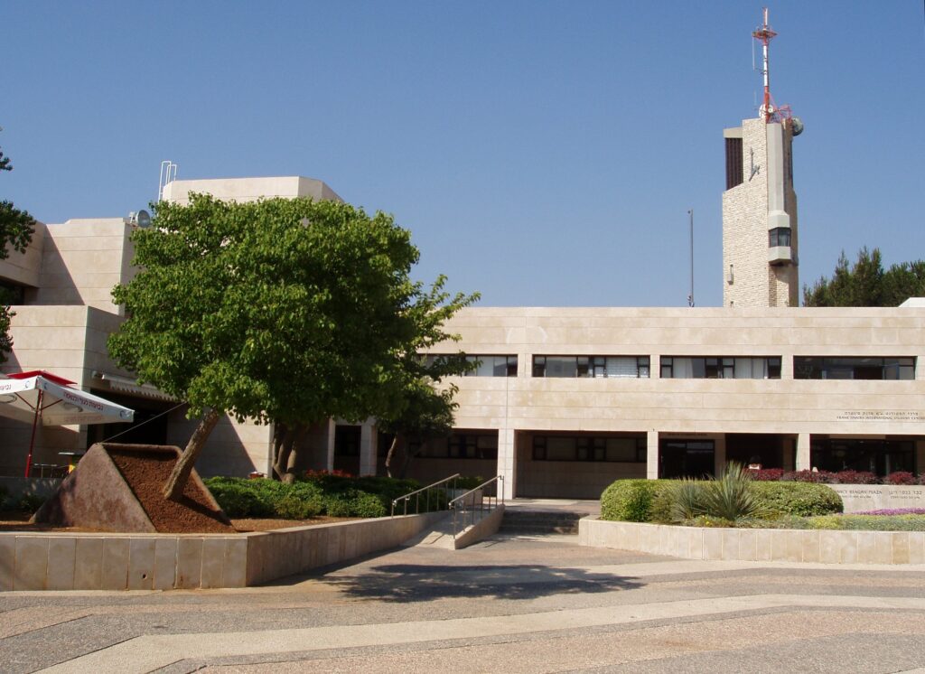 Prédios do campus Monte Scopus da Universidade Hebraica de Jerusalém, com torre ao fundo e jardim à frente.
